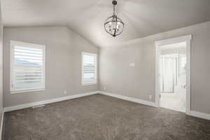 Empty room with a chandelier, baseboards, lofted ceiling, and carpet floors