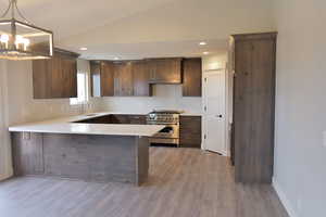 Kitchen featuring light countertops, a peninsula, vaulted ceiling, and stainless steel range