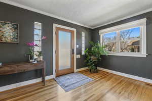 Foyer with visible vents, baseboards, wood finished floors, a textured ceiling, and crown molding