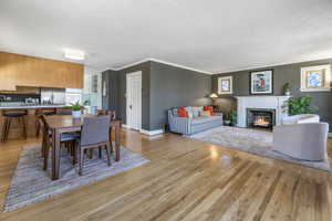 Dining room featuring baseboards, a fireplace with flush hearth, ornamental molding, a textured ceiling, and light wood-style floors