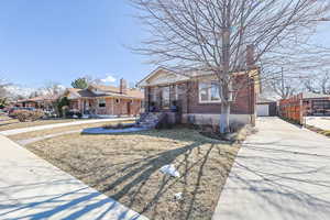 Bungalow featuring brick siding, a chimney, and an outbuilding