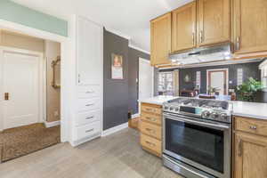 Kitchen featuring baseboards, light countertops, crown molding, under cabinet range hood, and gas stove