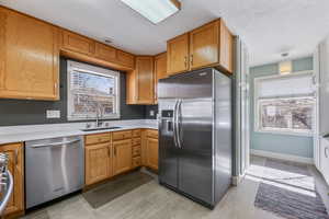 Kitchen with baseboards, brown cabinetry, stainless steel appliances, light countertops, and a sink