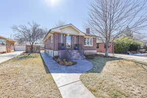 Bungalow-style house featuring a garage, brick siding, a chimney, fence, and a front yard