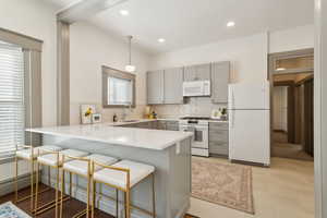 Open ktchen with tile backsplash, gray cabinets, light quartz countertops, white appliances, and large peninsula