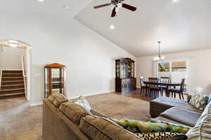 Carpeted living room featuring stairs, high vaulted ceiling, arched walkways, and baseboards