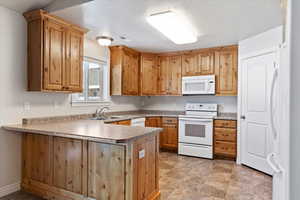 Kitchen featuring visible vents, brown cabinetry, a sink, white appliances, and a peninsula