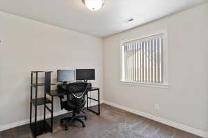 Carpeted home office with visible vents and baseboards