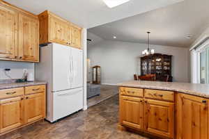 Kitchen with lofted ceiling, freestanding refrigerator, hanging light fixtures, light countertops, and a notable chandelier