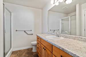 Bathroom featuring toilet, vanity, visible vents, baseboards, and a stall shower