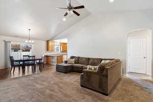 Living room with carpet floors, visible vents, high vaulted ceiling, baseboards, and ceiling fan with notable chandelier