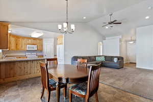 Carpeted dining space with baseboards, ceiling fan with notable chandelier, vaulted ceiling, a sink, and recessed lighting