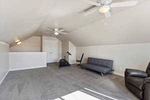 Living area featuring carpet floors, baseboards, vaulted ceiling, and a ceiling fan