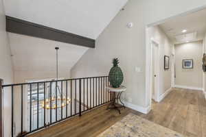 Hall with attic access, baseboards, wood finished floors, vaulted ceiling with beams, and an inviting chandelier