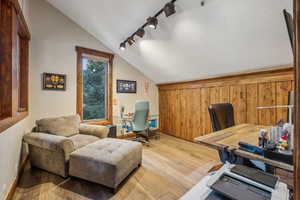 Office area featuring rail lighting, light wood-style flooring, vaulted ceiling, a textured ceiling, and baseboards