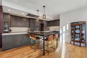 Kitchen featuring light wood-type flooring, backsplash, dark brown cabinetry, and decorative light fixtures