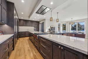 Kitchen with stainless steel gas cooktop, recessed lighting, light wood-style flooring, decorative backsplash, and light stone countertops