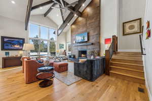 Living room with a large fireplace, visible vents, stairway, wood finished floors, and high vaulted ceiling