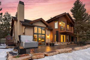 View of front of home with a patio, a chimney, stone siding, and a balcony