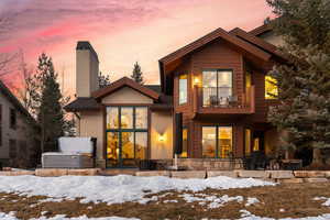 Snow covered back of property with a balcony, stone siding, and a chimney