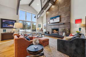 Living area with high vaulted ceiling, a tile fireplace, wood finished floors, and beam ceiling