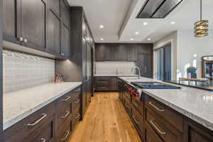 Kitchen with dark brown cabinetry, a sink, stainless steel gas stovetop, light wood finished floors, and pendant lighting