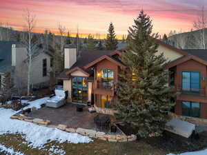 View of front of home featuring a patio, a chimney, stone siding, and a balcony