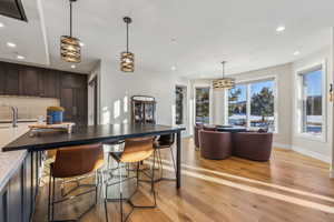 Kitchen with recessed lighting, decorative backsplash, dark brown cabinets, light wood-type flooring, and a kitchen bar