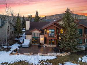 View of front of home with a chimney, a shingled roof, a patio area, a balcony, and stone siding