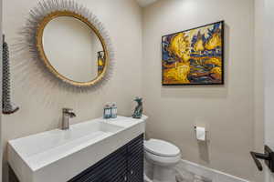 Half bathroom with toilet, baseboards, and vanity