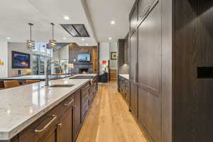 Kitchen featuring open floor plan, light stone countertops, light wood-style floors, a fireplace, and a sink