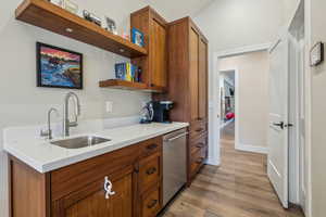 Kitchen with wood finished floors, a sink, stainless steel dishwasher, brown cabinets, and open shelves