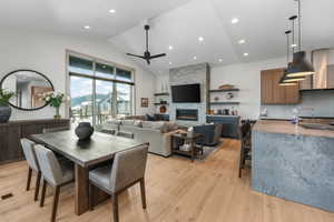 Dining space with light wood-style flooring, ceiling fan, a stone fireplace, high vaulted ceiling, and recessed lighting