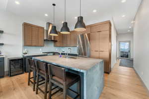 Kitchen with a kitchen island with sink, stainless steel appliances, light countertops, wall chimney range hood, and a sink