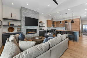 Living room with high vaulted ceiling, recessed lighting, a stone fireplace, and light wood finished floors