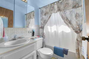 Full bath featuring tile walls, backsplash, toilet, shower / tub combo, and vanity
