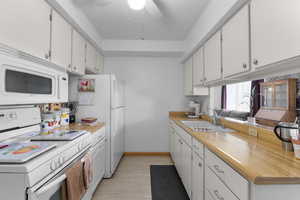 Kitchen featuring white appliances, light countertops, a sink, and white cabinetry