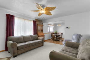 Living room featuring a textured ceiling, ceiling fan with notable chandelier, wood finished floors, and baseboards
