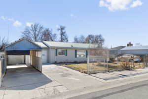 Single story home with driveway, fence, metal roof, and a carport
