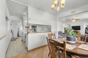 Dining space with light wood-type flooring, baseboards, and ceiling fan with notable chandelier