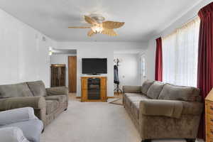 Living area featuring ceiling fan, visible vents, and light colored carpet