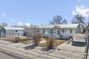 View of front facade featuring driveway, a fenced front yard, a gate, and metal roof
