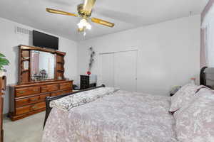 Bedroom with visible vents, a ceiling fan, carpet, a textured ceiling, and a closet