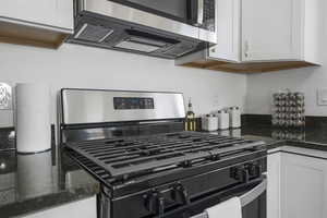 Kitchen featuring stainless steel appliances, dark countertops, and white cabinetry