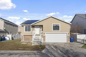 View of front facade featuring stone siding, fence, roof mounted solar panels, and stucco siding