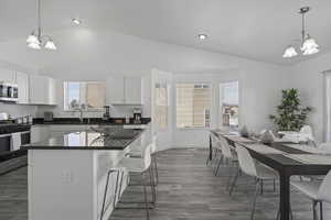 Kitchen featuring a chandelier, a breakfast bar area, white cabinetry, appliances with stainless steel finishes, and dark countertops