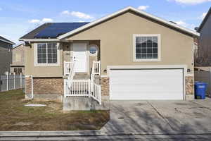 View of front facade with stone siding, fence, roof mounted solar panels, and stucco siding