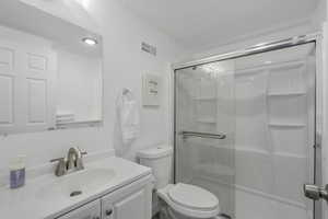 Full bath with visible vents, toilet, a textured ceiling, a shower stall, and vanity