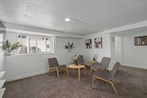 Living area featuring carpet flooring, a paneled ceiling, and baseboards