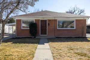 Front door featuring brick siding, a lawn, and a new roof